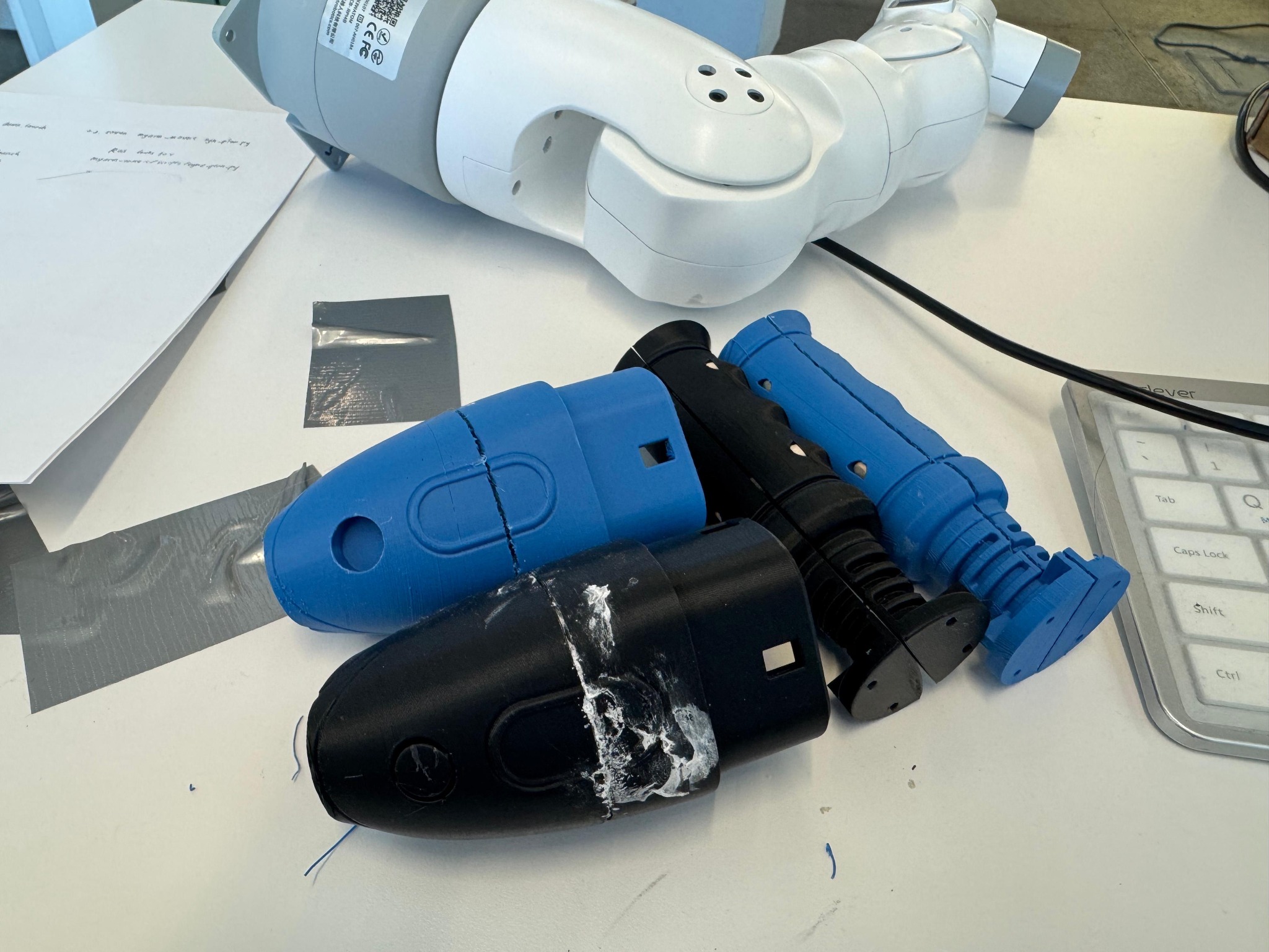 Several blue and black 3D-printed end-effector concepts arranged beside a robotic arm.